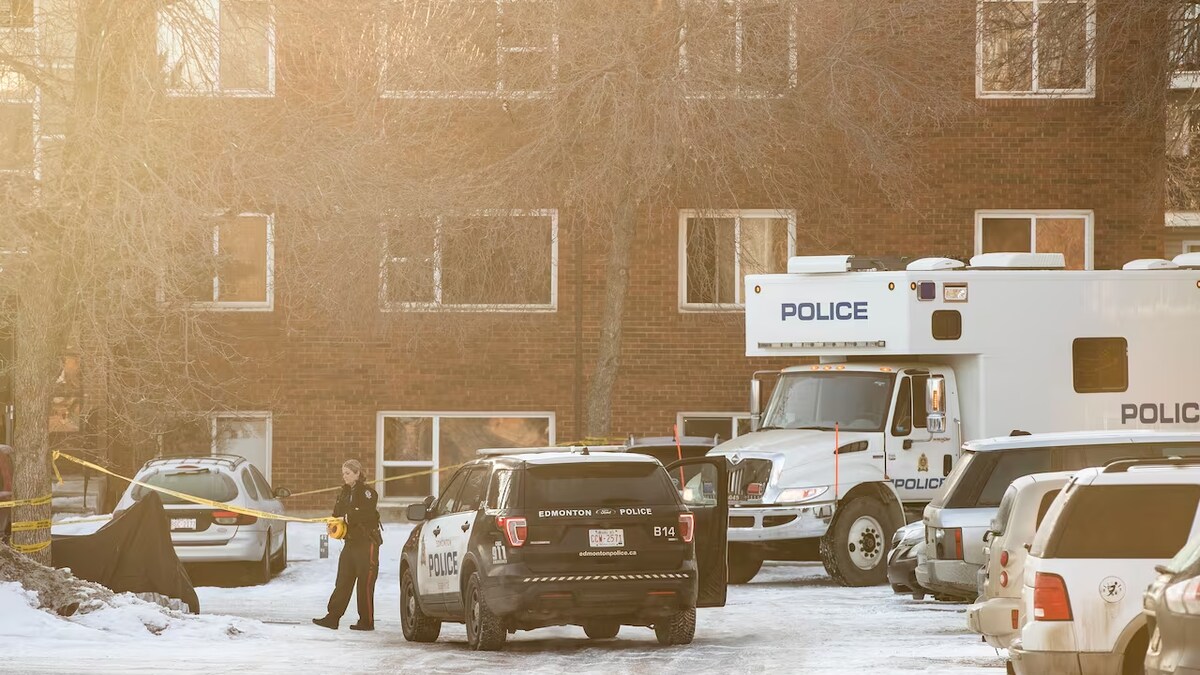 Une policière, près d'un véhicule de police d'Edmonton, déroule un ruban pour délimiter une zone.
