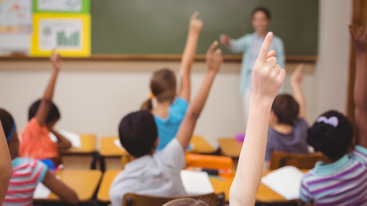 Une enseignante pose une question et les élèves lèvent la main pour répondre.