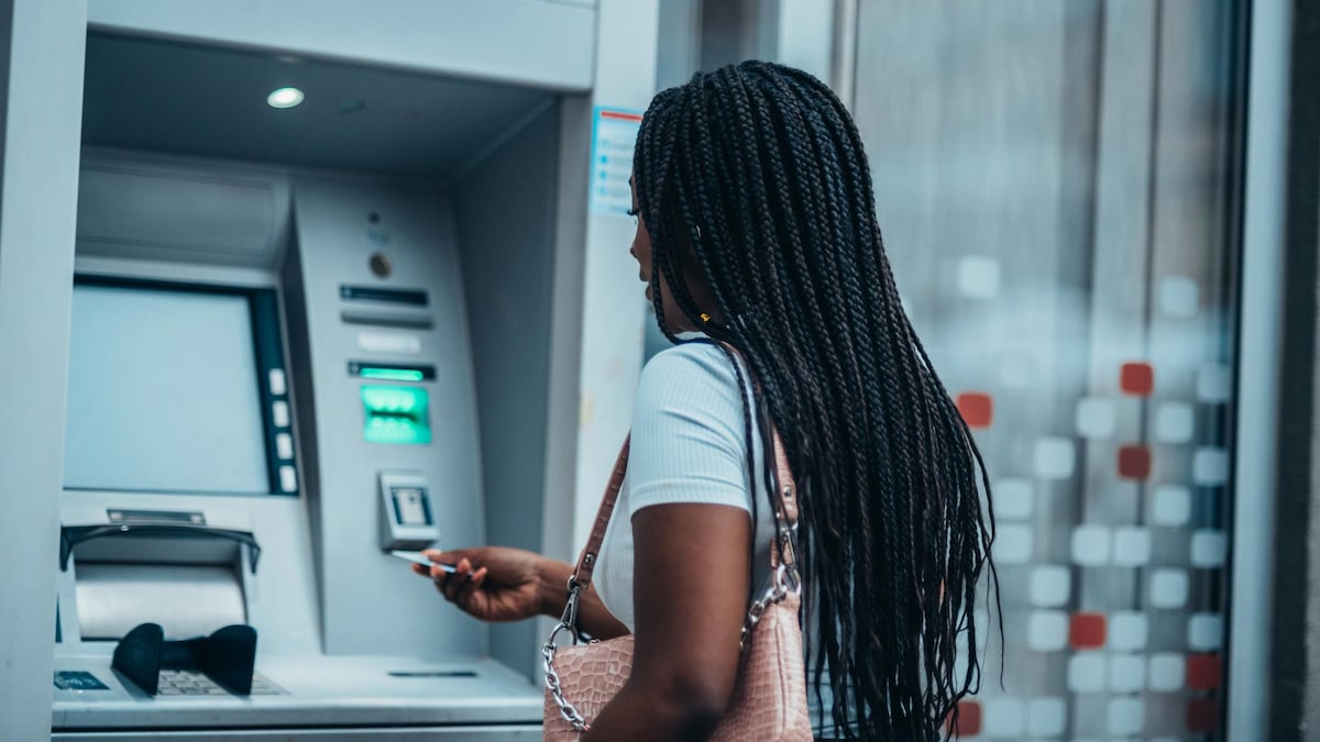 Une femme s'apprête à insérer sa carte dans un guichet automatique bancaire.