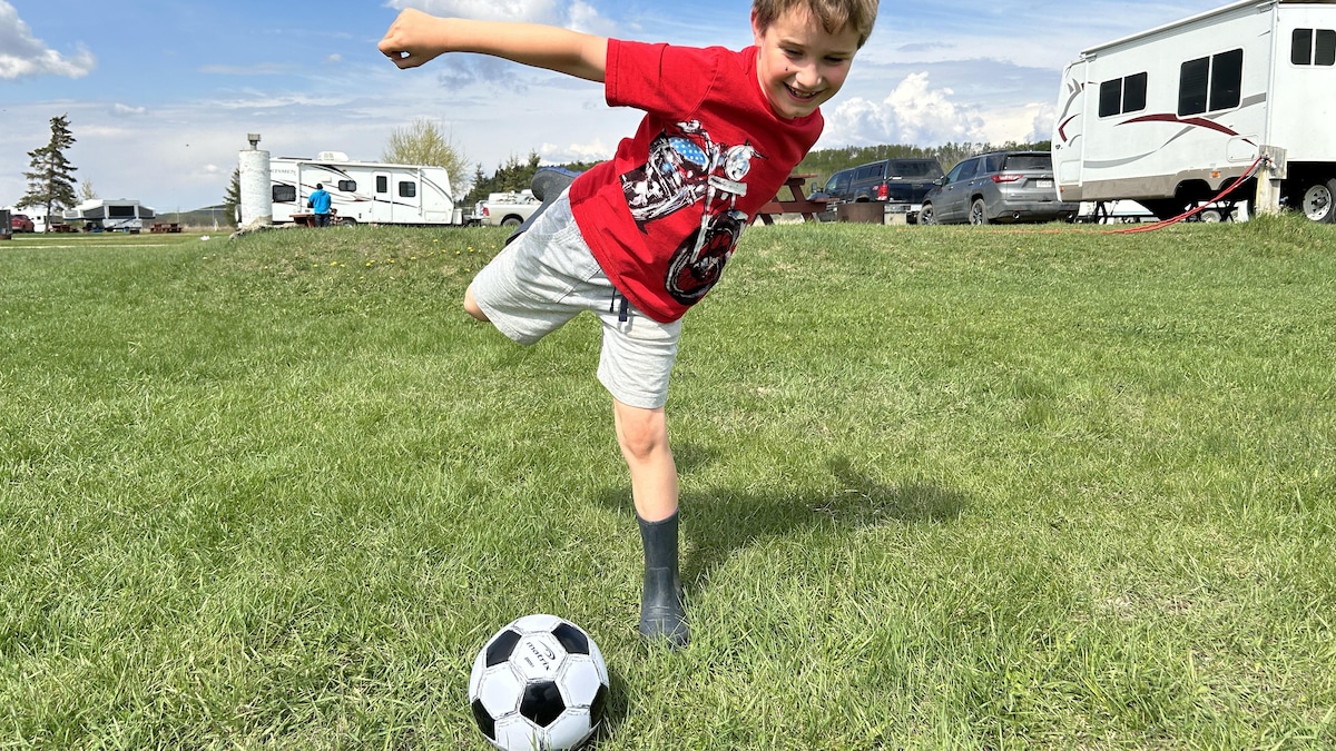 Un jeune garçon donne un coup de pied à un ballon de soccer à l'extérieur lors d'une journée ensoleillée.