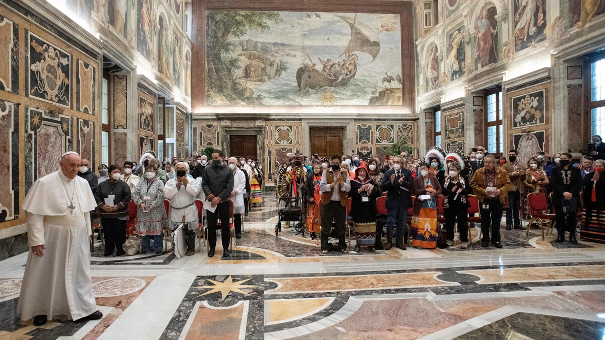 Le pape et, en arrière-plan, plusieurs personnes debout dans une vaste pièce du Vatican. 