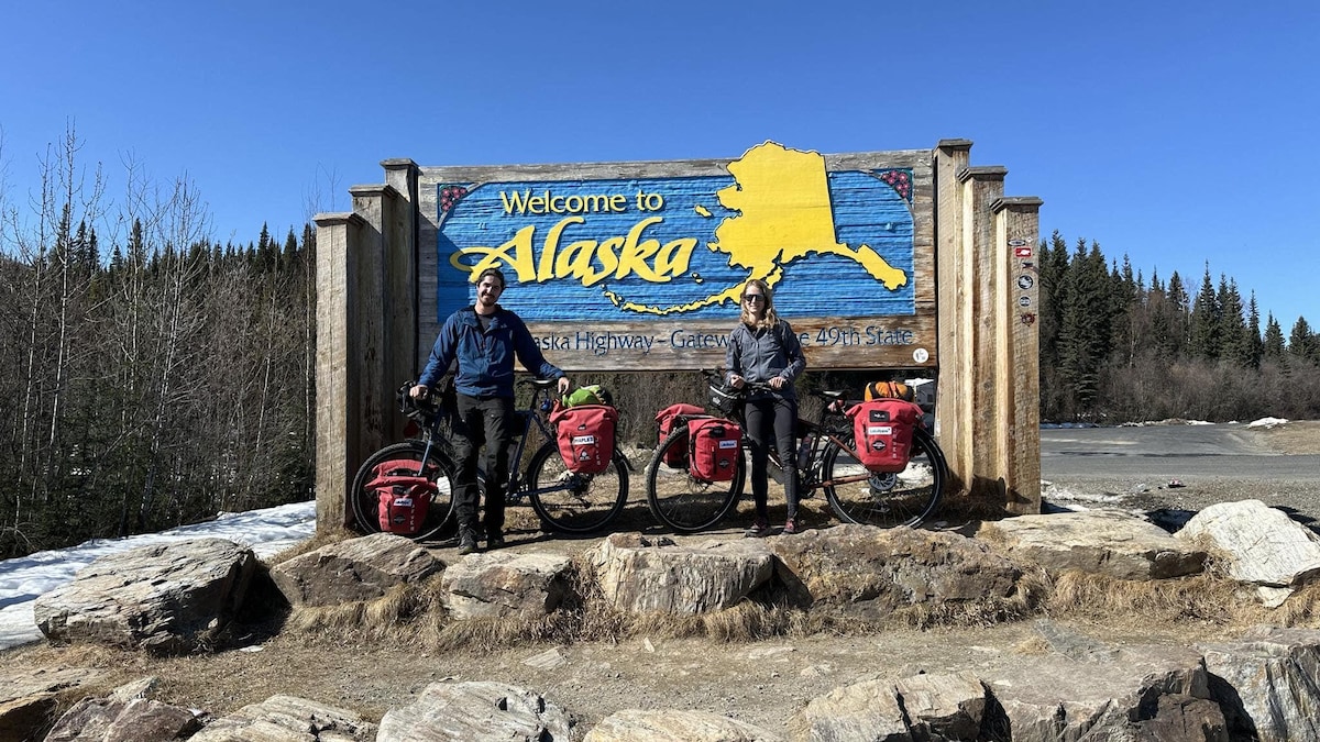 Ils posent avec leurs vélos devant une grande enseigne «Welcome to Alaska».