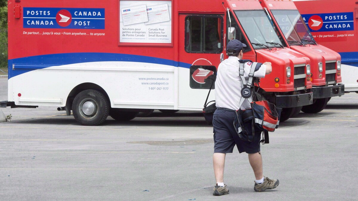 Un postier passe devant les camions de Postes Canada dans un centre de tri.