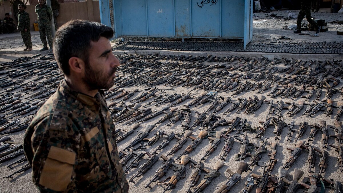 Un membre des Forces démocratiques syriennes se tient des centaines d'armes déposées sur le sol. 