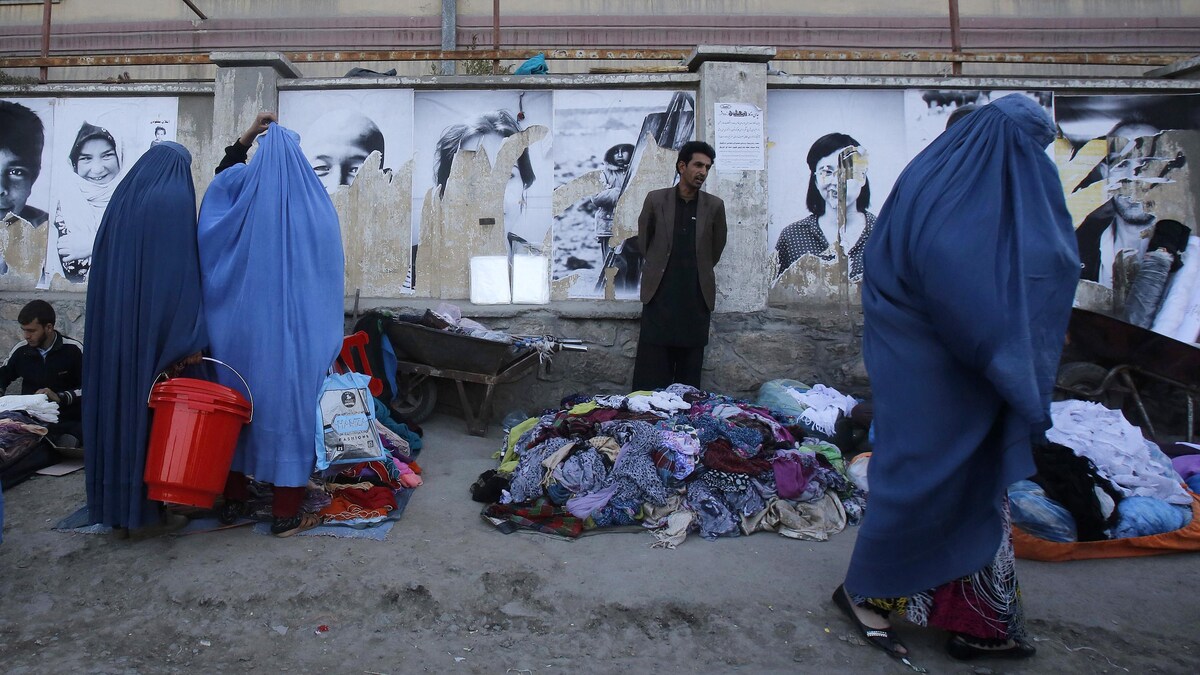 Des vendeurs se tiennent derrière des tas de vêtements, les femmes portent la burqa.