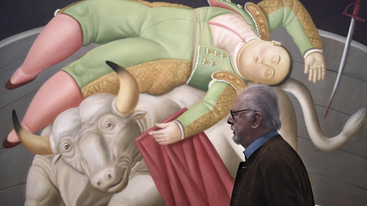 L'homme est photographié de profil marchant devant une peinture montrant un toréador mort sur un taureau. 