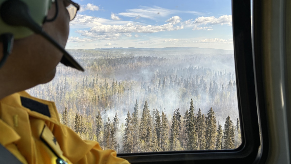 Une personne dans un hélicoptère regarde la fumée sortant d'une forêt, en mai 2024.