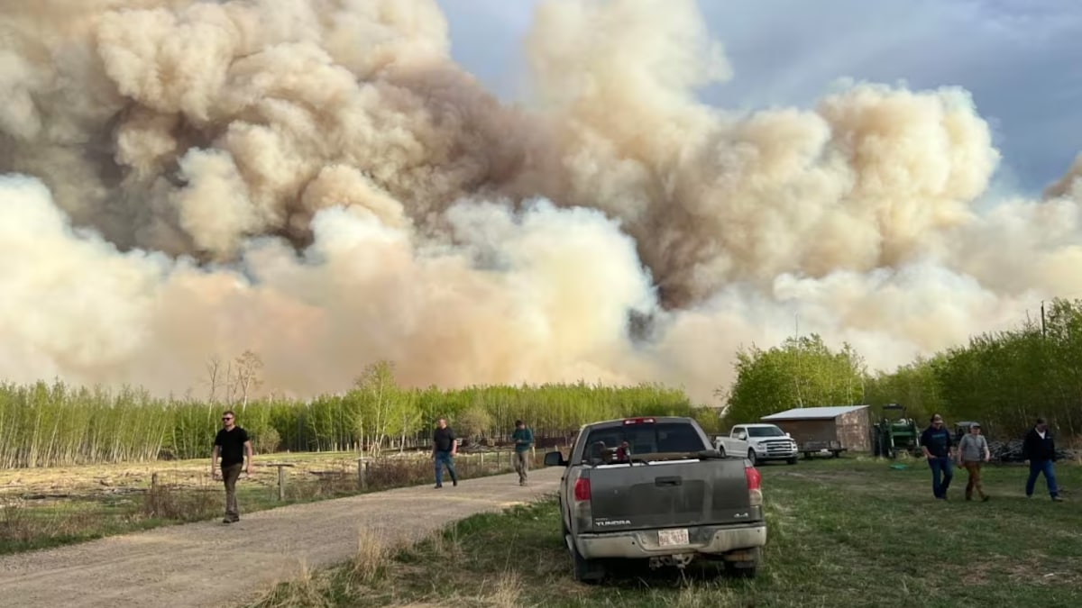 Des personnes et véhicules sur une ferme en premier plan, et en arrière-plan, la fumée couvre le ciel. 
