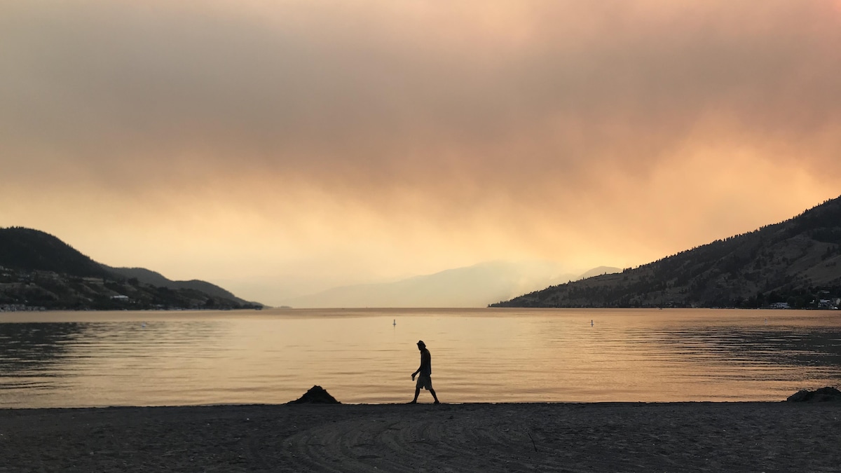 Une personne qui marche sur la plage sous un ciel rouge et brumeux.