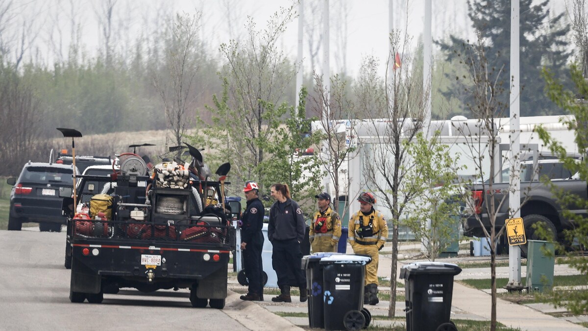 Un camion transportant du matériel est stationné dans la rue d'un quartier résidentiel, des personnes en uniformes du service des incendies se tiennent debout à côté, le 15 mai 2024.