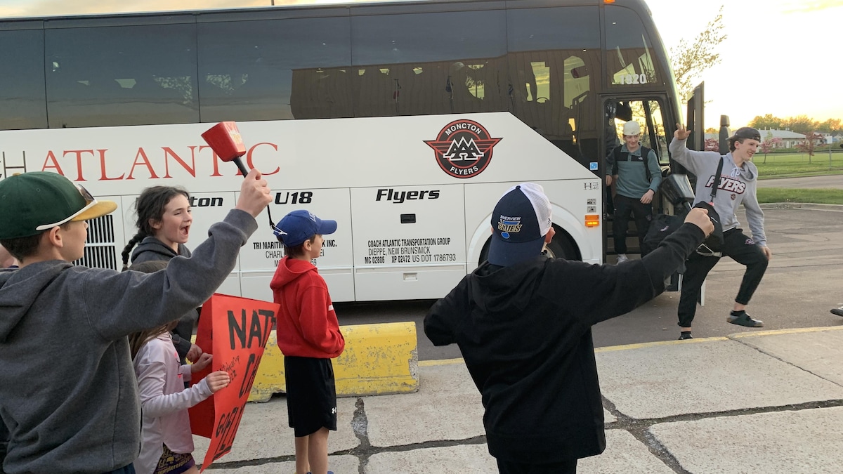 Des supporteurs d’une équipe de hockey sont tout sourire en voyant l’autobus des joueurs arrivé. 