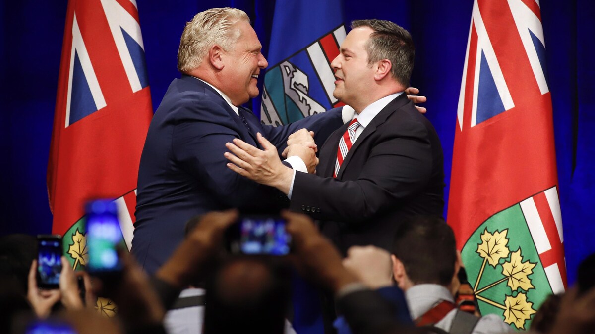 Le premier ministre de l'Ontario, Doug Ford, et le chef du Parti conservateur uni de l'Alberta, Jason Kenney (à gauche), se félicitent autour de deux drapeaux lors d'un rassemblement contre la taxe carbone à Calgary.