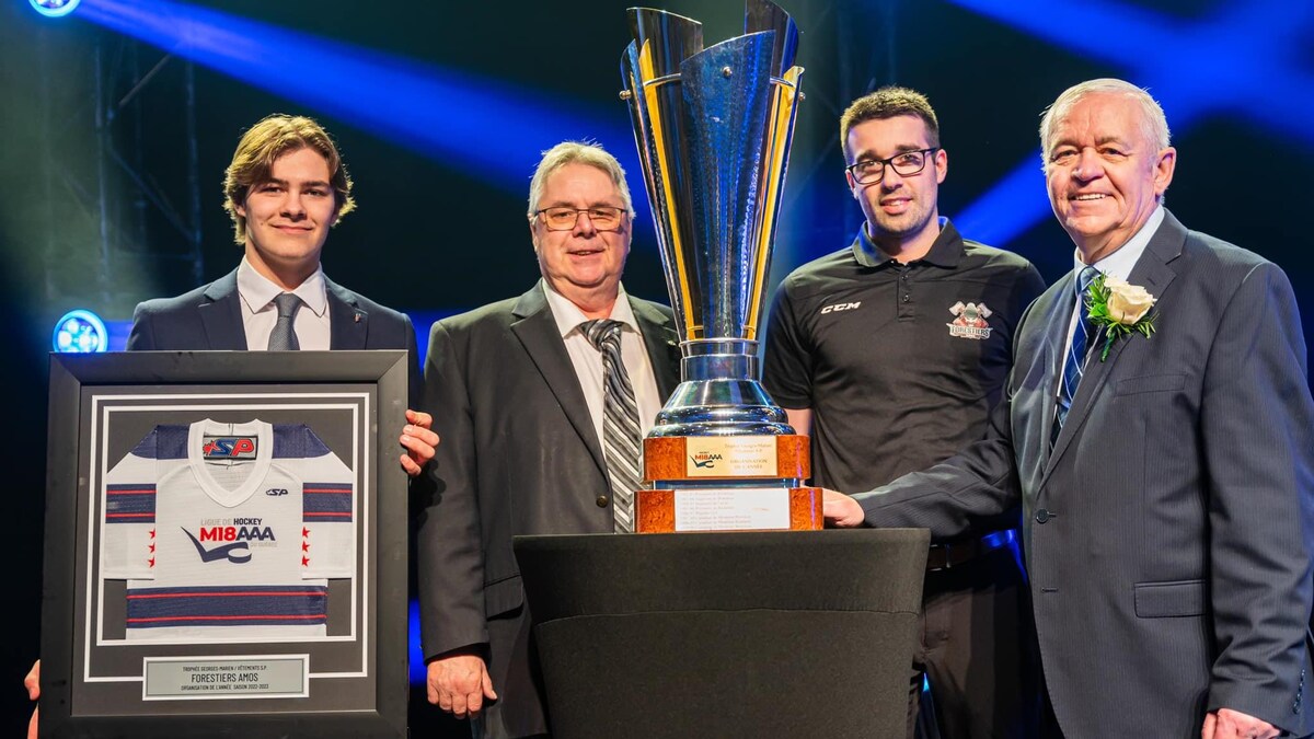 Quatre hommes posent avec un gros trophée et une plaque honorifique.