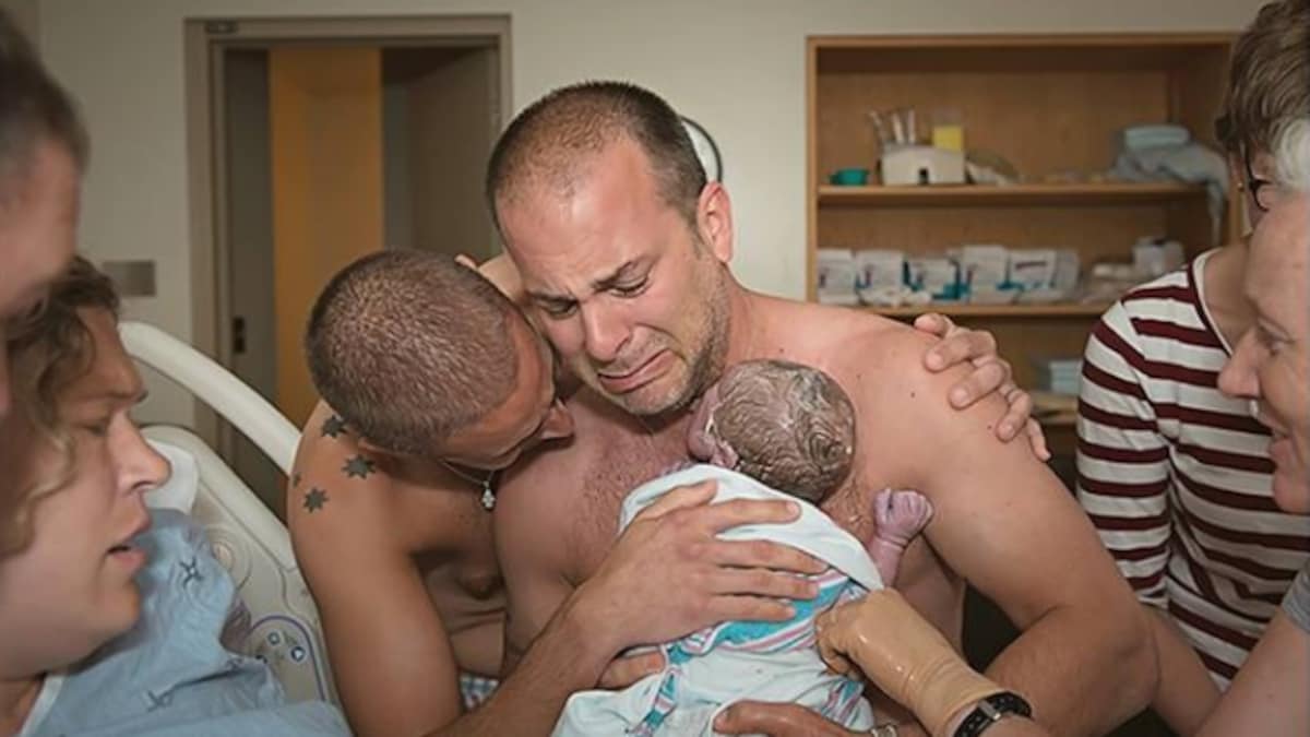 Frankie Nelson tient son fils contre sa poitrine en pleurant dans une salle d'accouchement. Son conjoint, BJ Barone, le tient par l'épaule. Ils sont entourés de la femme qui a porté leur enfant et d'infirmières.