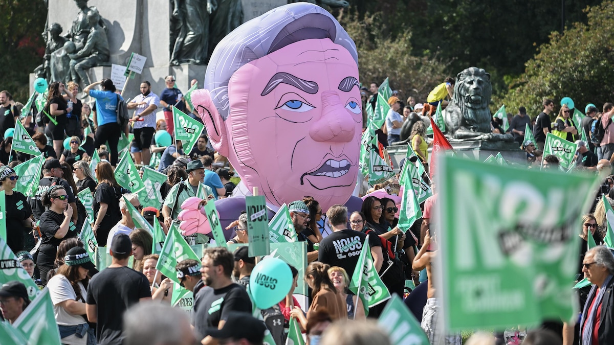 Des manifestants sont regroupés, alors qu'une géante tête de François Legault gonflable flotte.