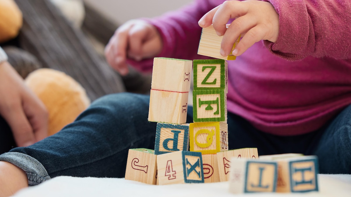 Un jeune enfant assis par terre joue avec des blocs sur lesquels des lettres sont écrites.