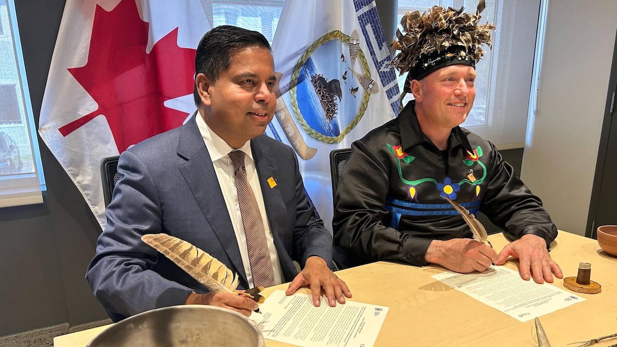 Le ministre Gary Anandasangaree et le grand chef Rémy Vincent signent un document devant un drapeau du Canada et un drapeau de la Nation huronne-wendat.