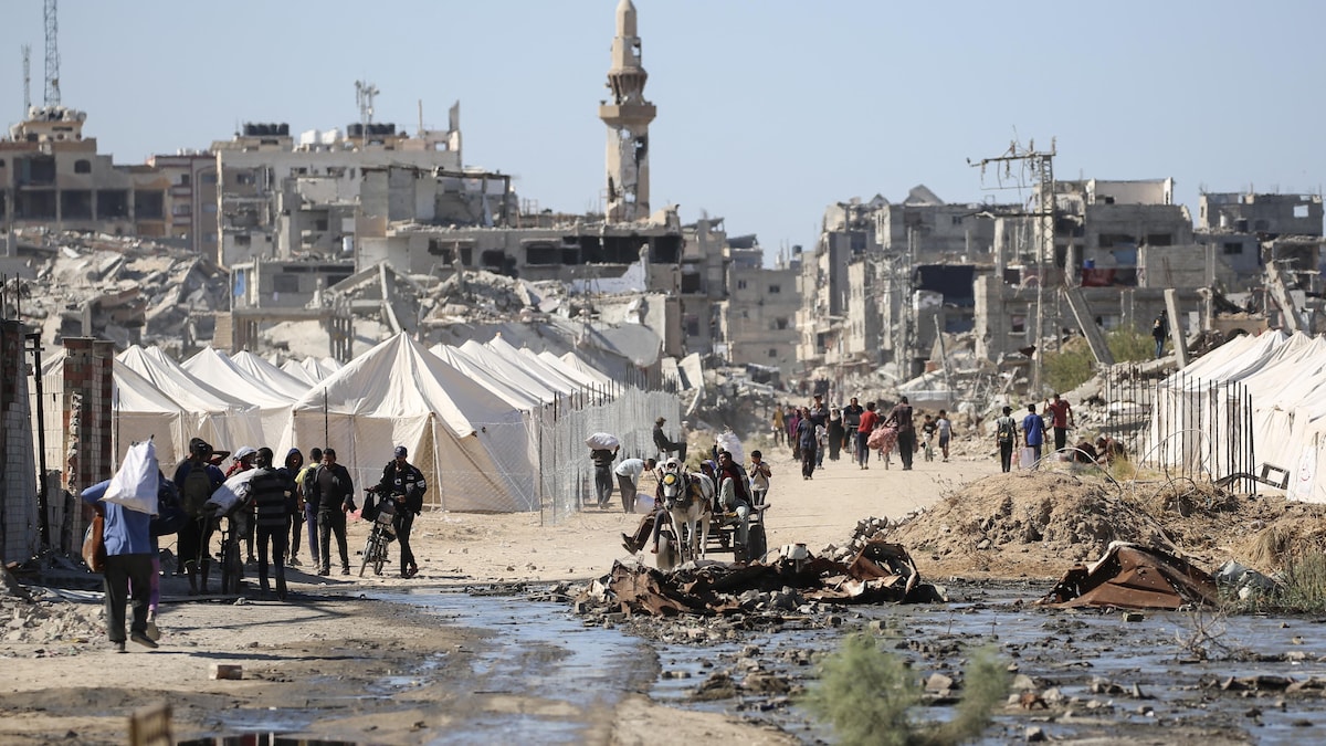 Des Palestiniens déplacés passent devant des tentes et des bâtiments détruits.