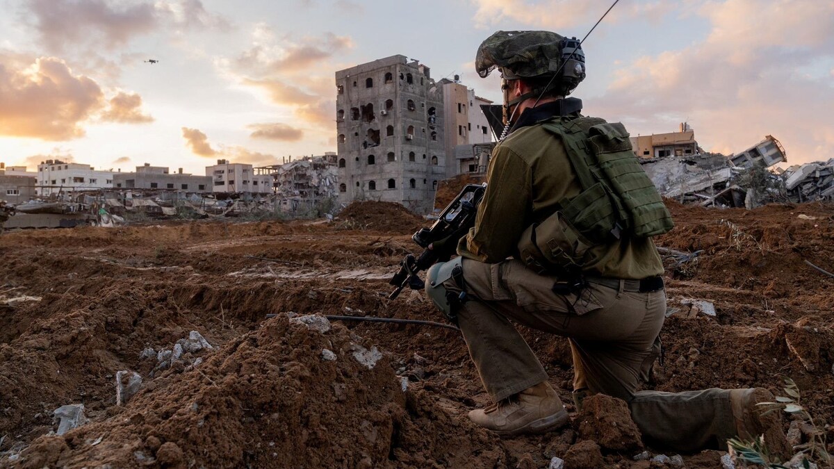 Un soldat armé, le genou à terre, parmi des décombres d'immeubles.