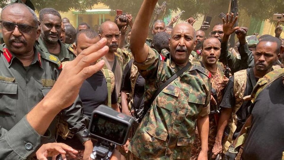 Le général Abdel Fattah al-Burhane, en uniforme militaire et entouré de soldats, lève un bras vers le ciel. 