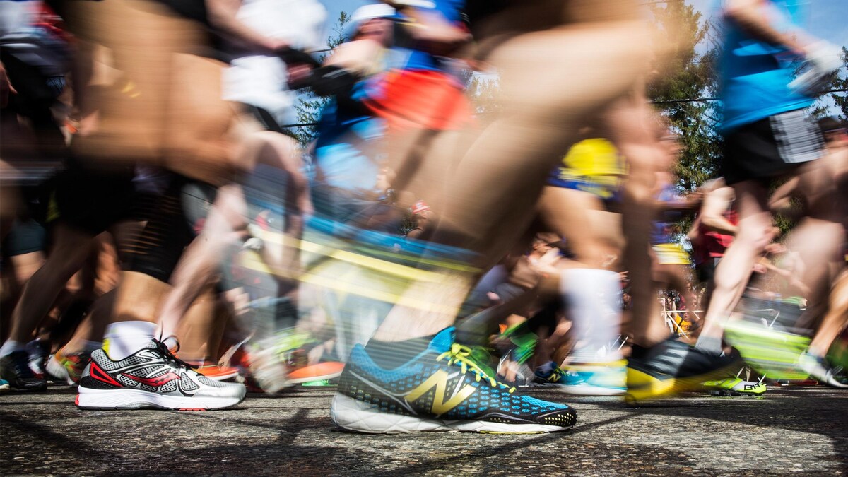 Focus sur un soulier de marque New Balance, en avant-plan. À l'arrière, les pas et les souliers de la foule de coureurs sont flous.