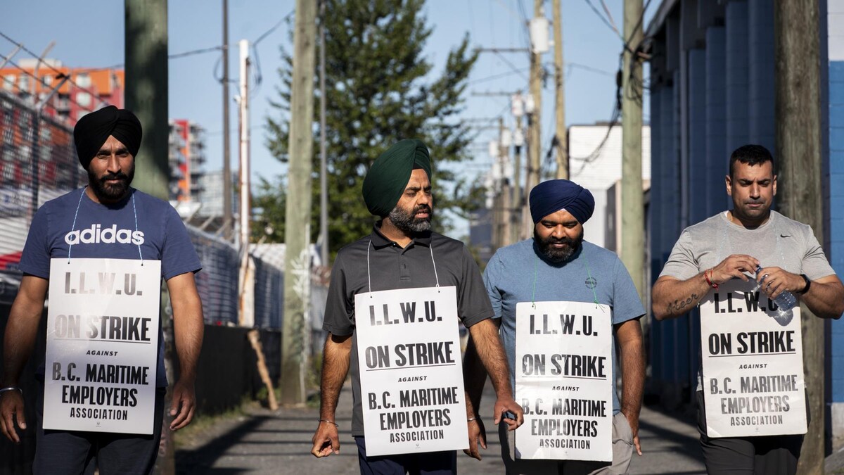 Quatre employés du port de Vancouver marchent avec des pancartes le 19 juillet 2023.