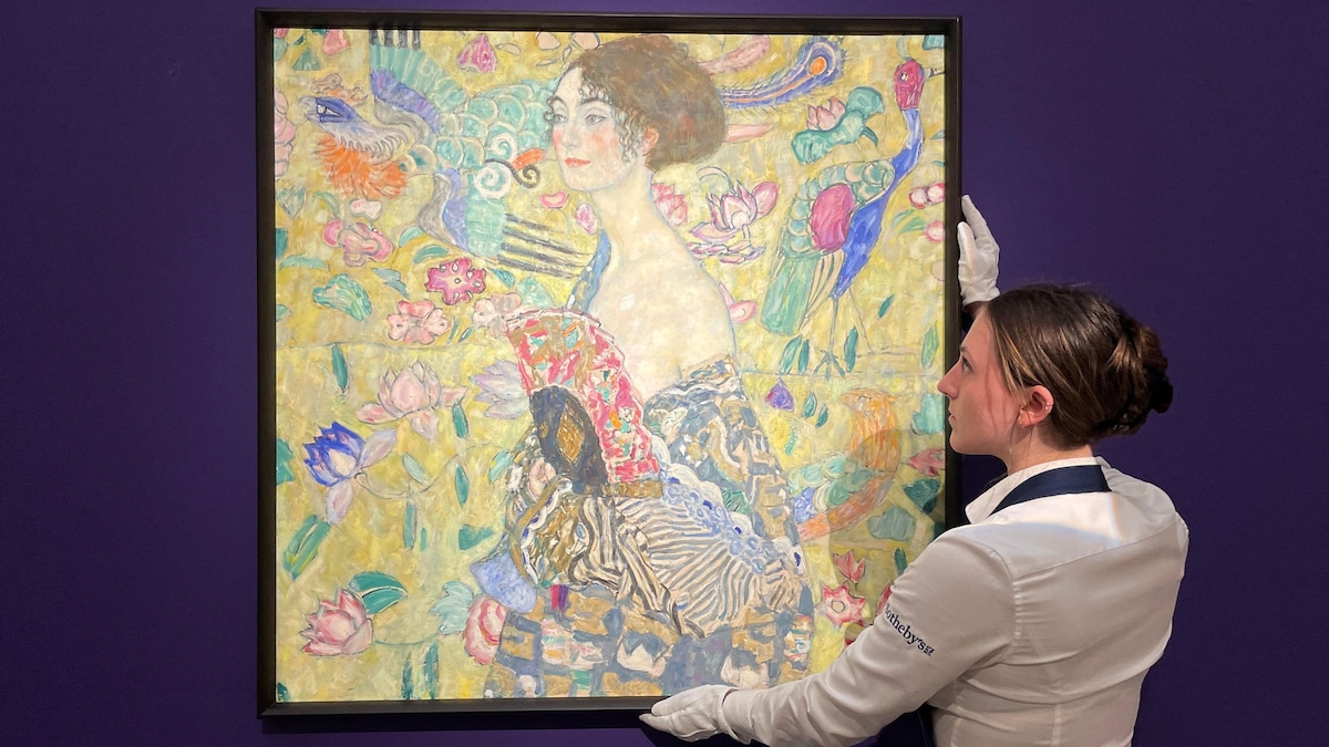 Une employée pose la toile de Klimt sur un mur bleu. 