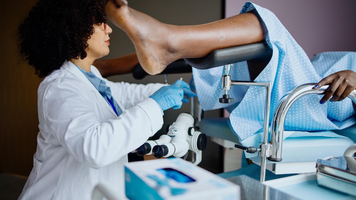 Une patiente allongée sur une table, les pieds dans des étriers, en train de subir un test Pap.