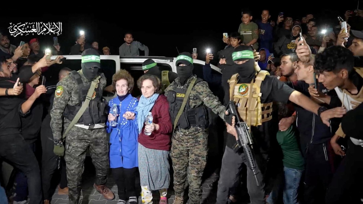 Des hommes armés et masqués entourent deux femmes. Une foule regarde.