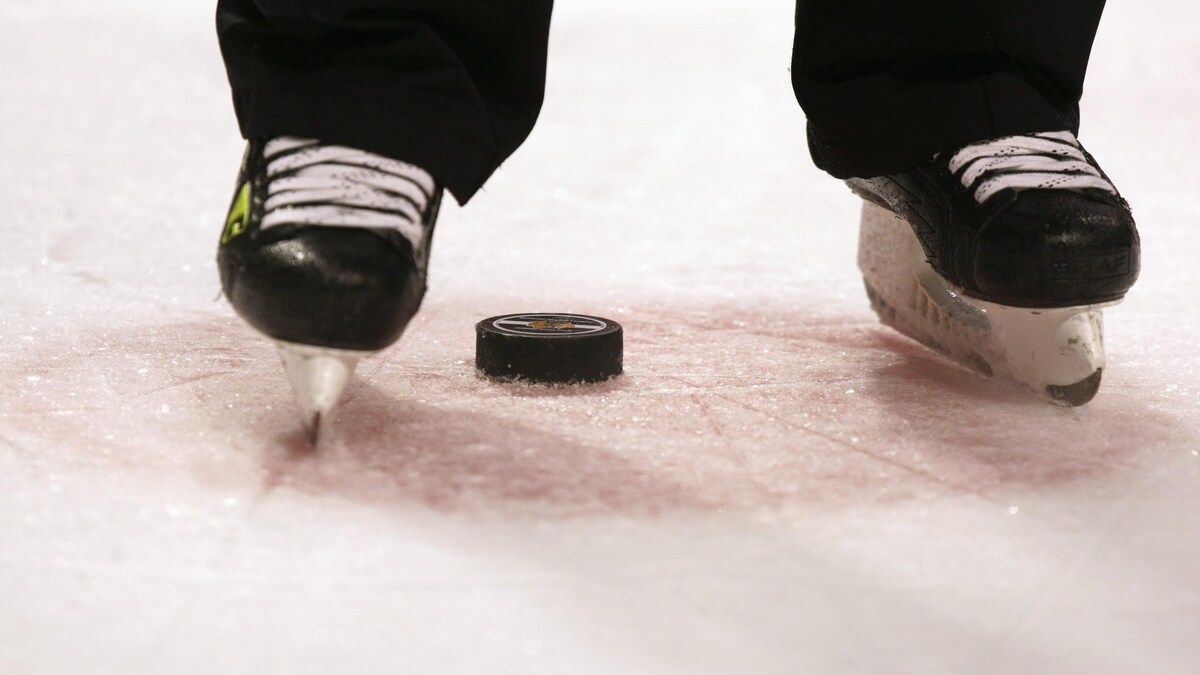 Une rondelle de hockey sur une patinoire, entre les patins d'un arbitre.