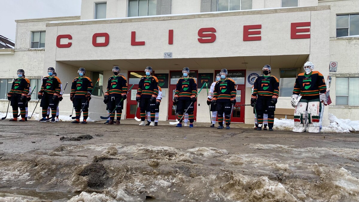 Les joueurs de l'équipe de hockey Les Patriotes vêtus de leur équipement posent devant le colisée de Trois-Rivières