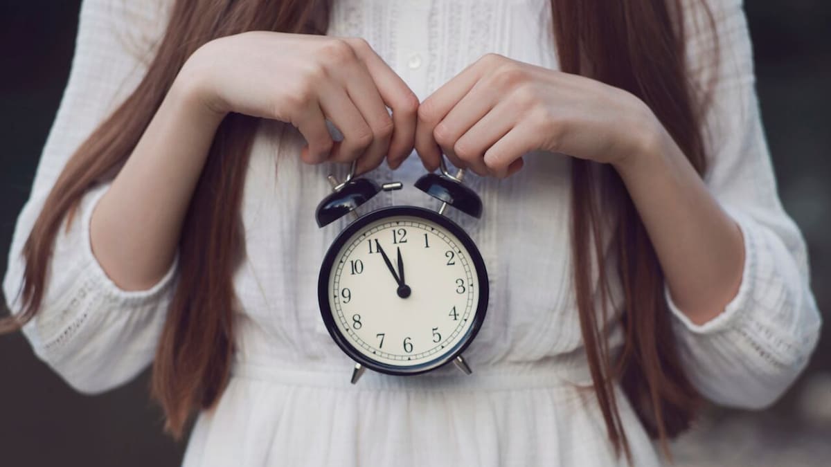 Une femme tient une horloge qui affiche minuit moins cinq minutes avec les deux mains. 