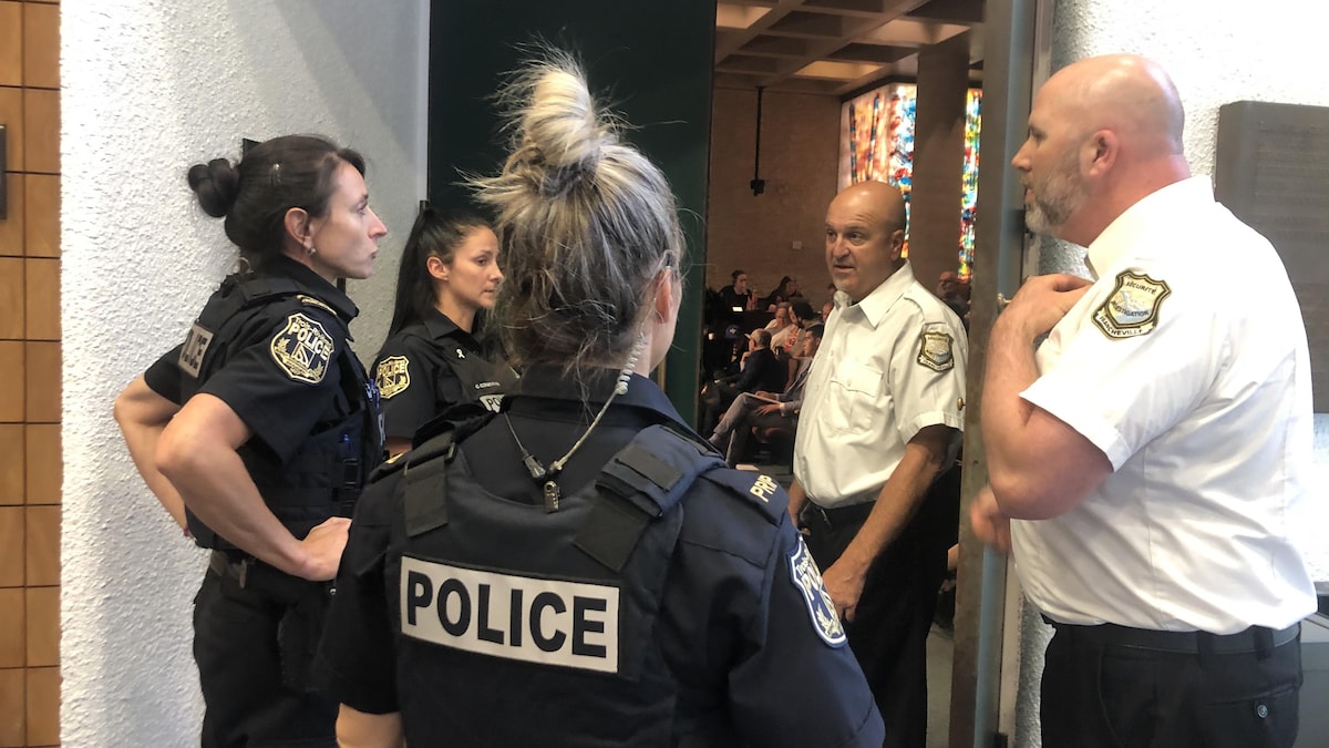 Des policières discutent avec des gardiens de sécurité devant l'entrée de la salle du conseil municipal de Trois-Rivières.