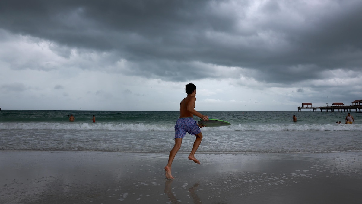 Un jeune homme en maillot court sur une plage, avec une planche de surf dans les mains, alors qu'il fait sombre.