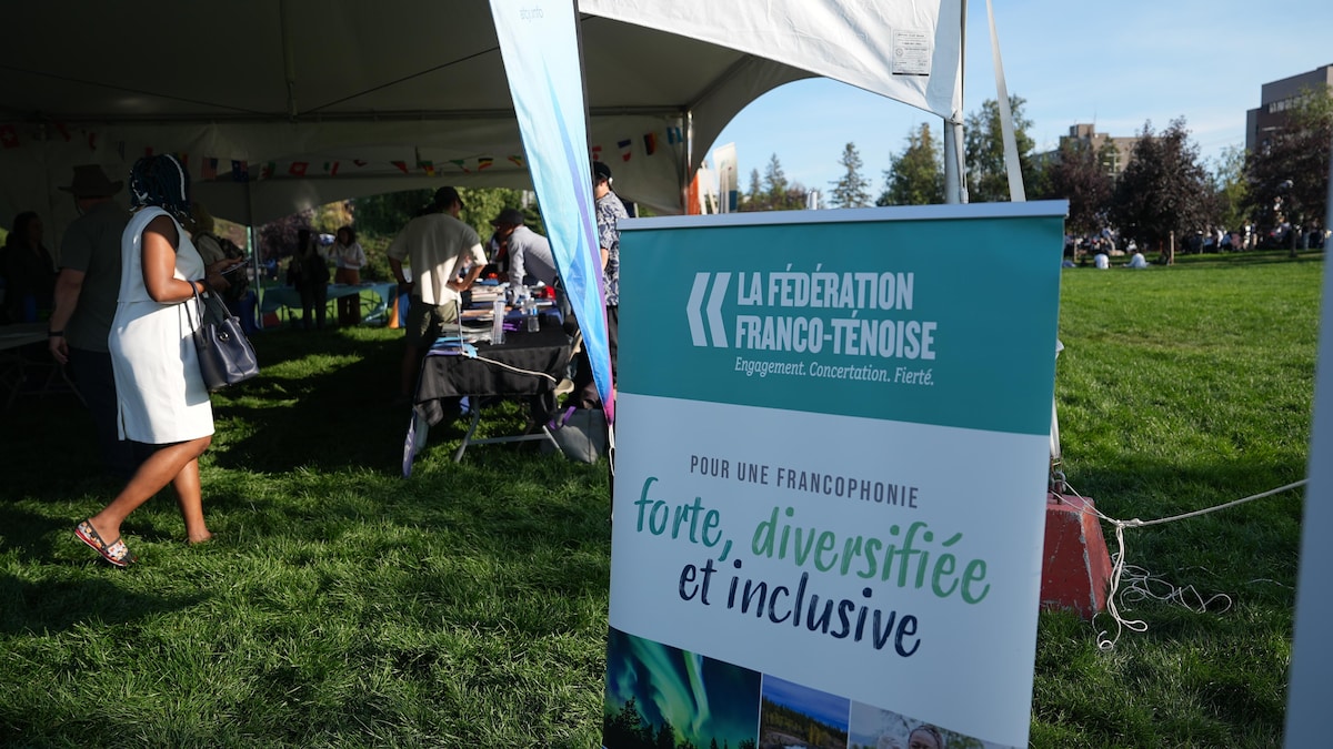 Un panneau de la Fédération franco-ténoise devant une tente abritant des exposants.