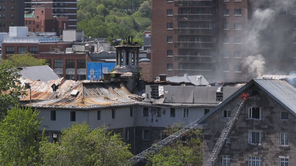 Deux grandes échelles de pompier dirigées vers une section du bâtiment d'où émerge une colonne de fumée.