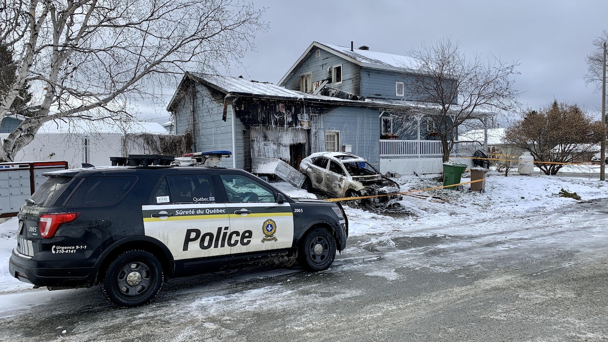 Un véhicule de police devant la voiture et la maison incendiées.