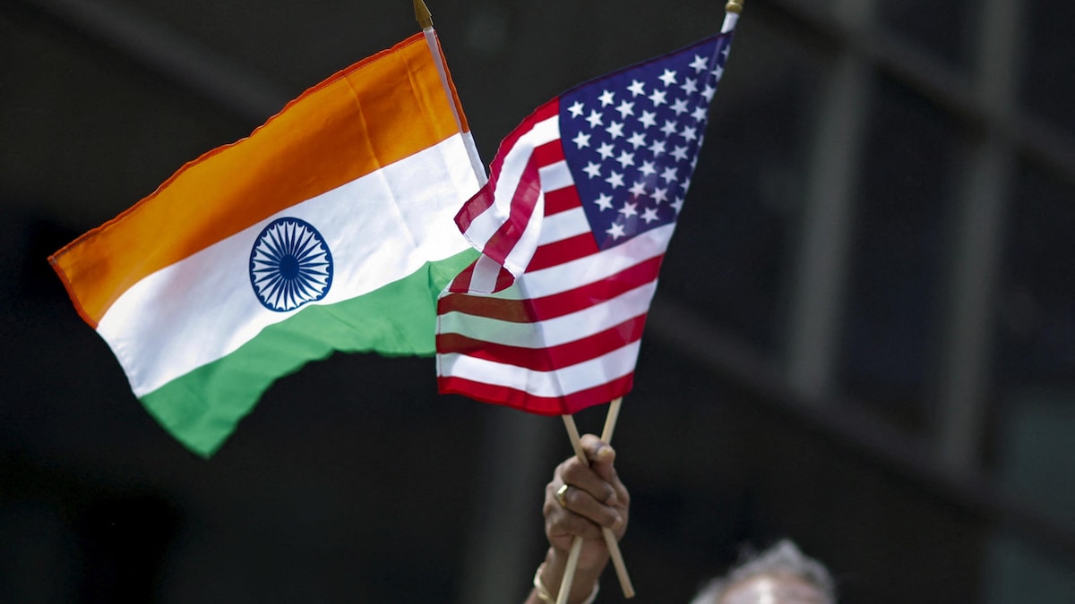 Un homme tient les drapeaux de l'Inde et des États-Unis dans sa main, haut levé.