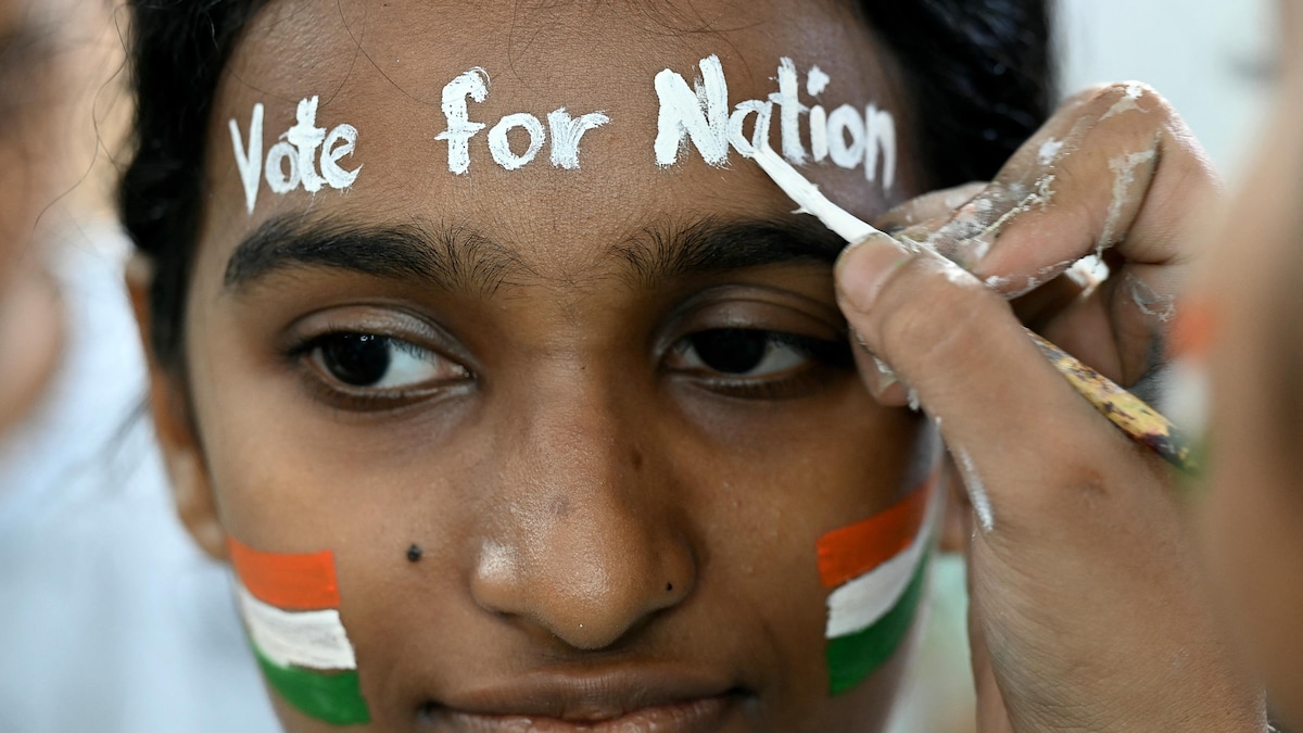 Une jeune femme qui a des drapeaux de l'Inde peints sur les joues se fait peindre sur le front un message indiquant «Votez pour la nation».