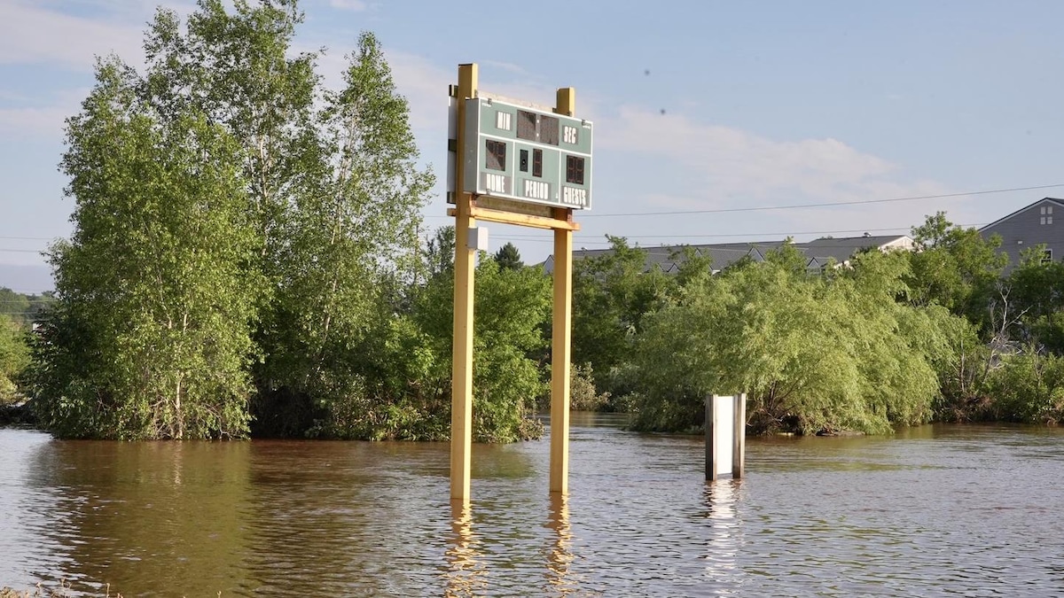Un tableau indicateur monté sur des poutres en bois hautes de plusieurs mètres émerge au-dessus d'un terrain de sport submergé par l'eau pendant une inondation.