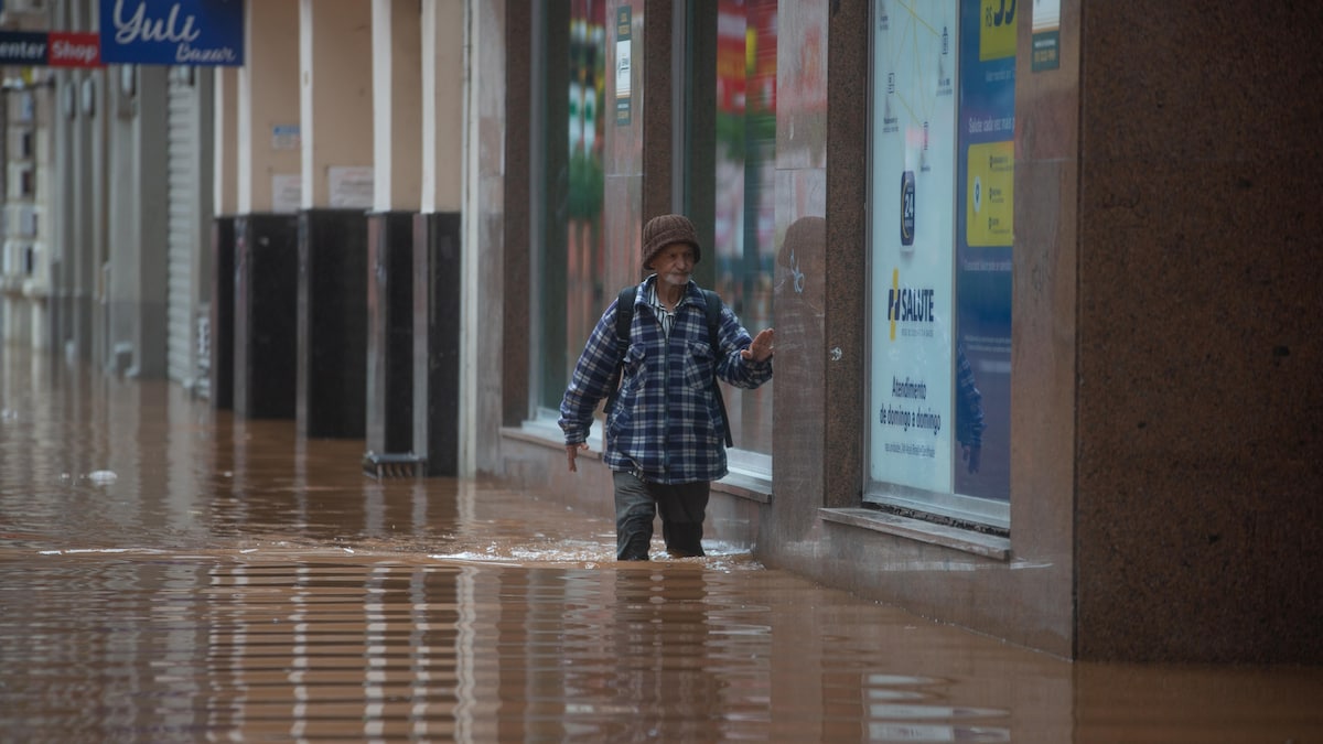 Un homme marche dans une rue commerçante, avec de l'eau jusqu'aux genoux. 