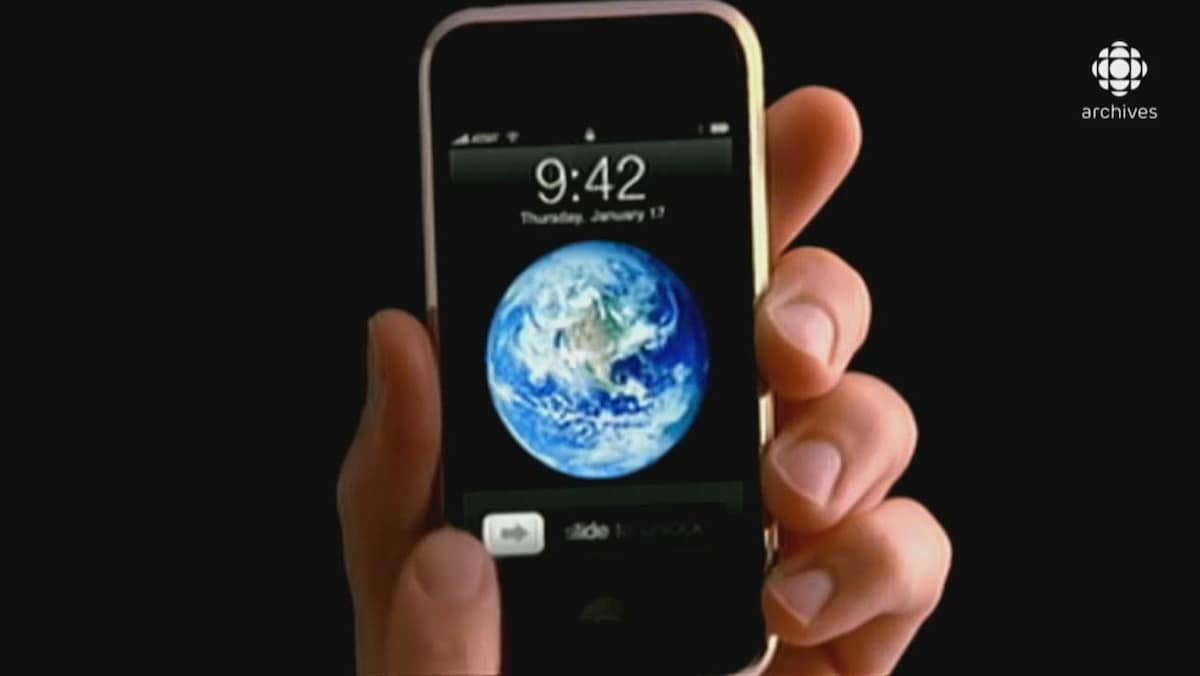Main tenant un appareil iPhone ouvert sur l'écran d'accueil affichant l'heure et une image de planète