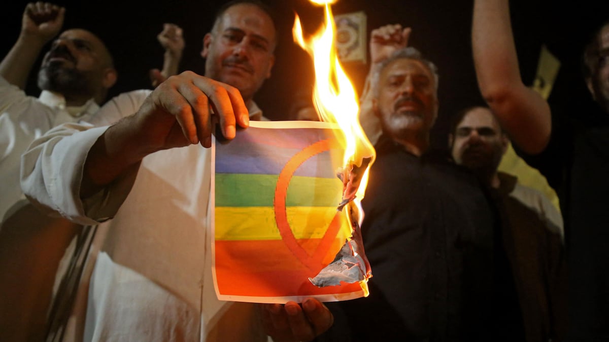 Un homme dans une foule tient une feuille en train de brûler avec le drapeau LGBTQ+ avec un signe rouge d'interdiction dessus.