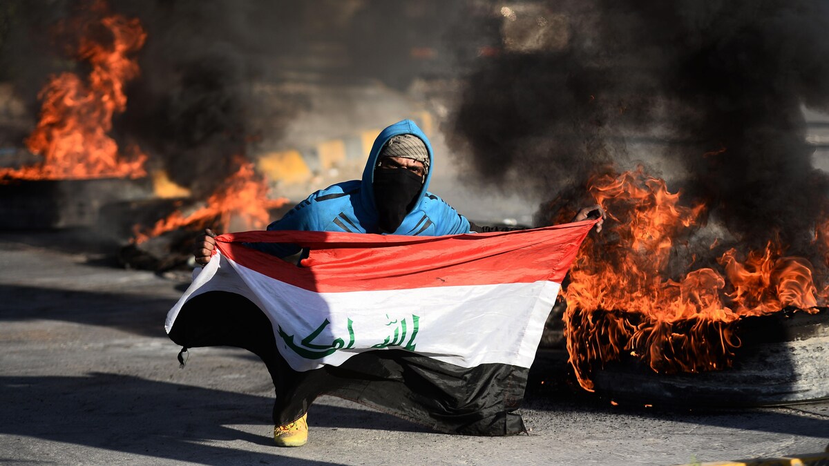 Un protestant irakien tient un drapeau dans un décor enflammé. 