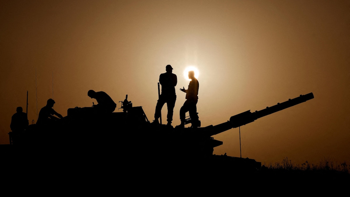 Des soldats sont debout sur un tank, à contre-jour, au coucher du soleil.