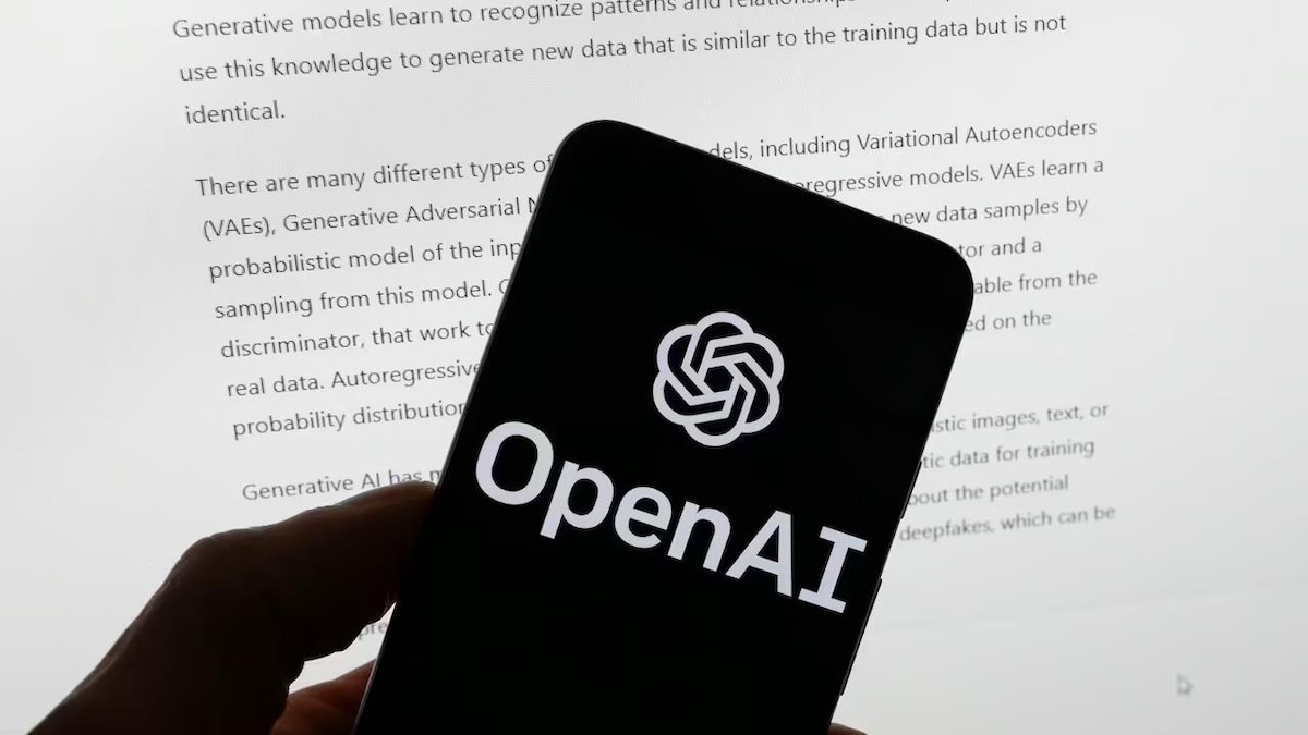 A hand holds a phone with OpenAI app in front of a computer screen on the ChatGPT page.