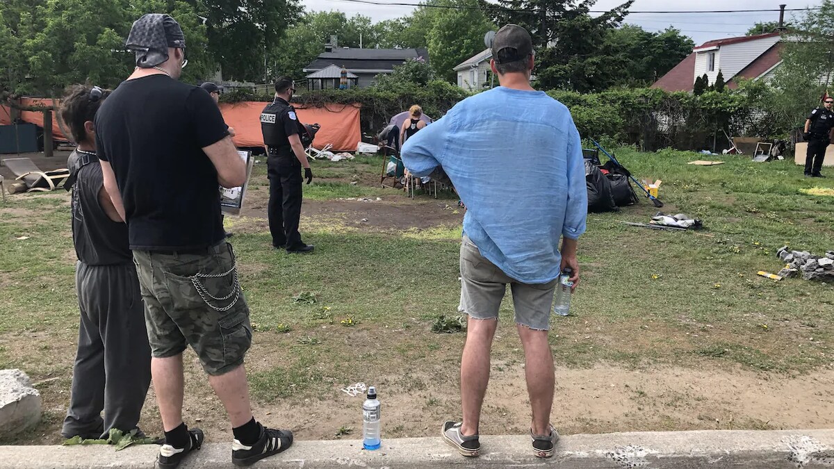 Un homme regarde des policiers démanteler un campement improvisé à l'extérieur. 