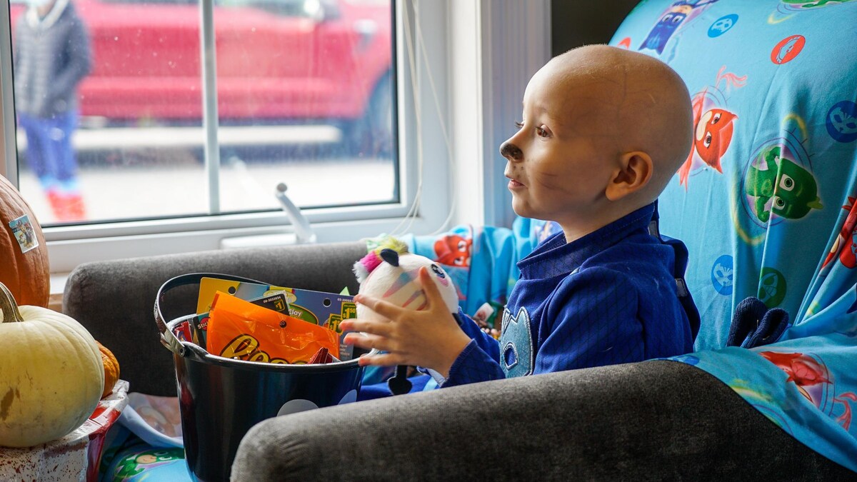 Un enfant avec la tête rasée en raison de traitement contre le cancer est assis dans un fauteuil devant une chaudière avec des bonbons.