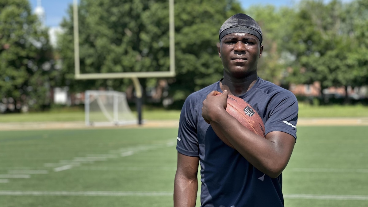 Un jeune homme tient un ballon sur un terrain de football.