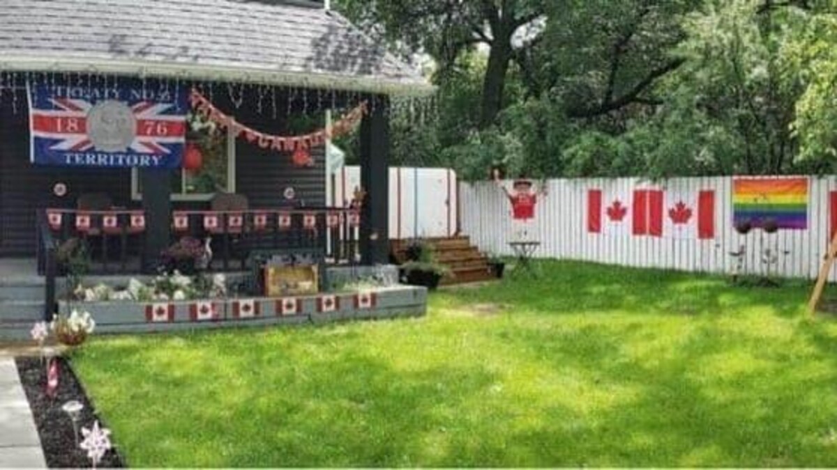La cour avant d'une maison est décorée avec des drapeaux canadiens et des guirlandes. Un drapeau du Traité 6 est suspendu sous le porche. Un drapeau de la Fierté est apposé sur une clôture.